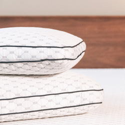 Two thick white pillows with dark gray piping stacked on top of each other.