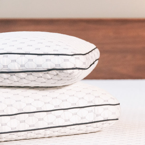 Two thick white pillows with dark gray piping stacked on top of each other. (No Script)