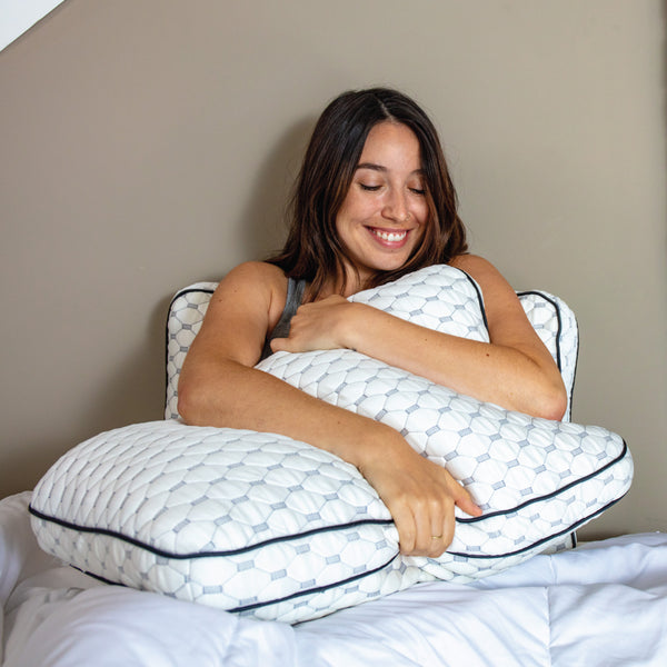 Woman smiling and hugging a thick white memory foam pillow to her chest while leaning against another pillow. (No Script, Alternate View)