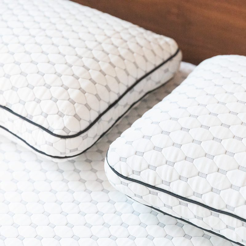 Two thick white pillows on a bed.
