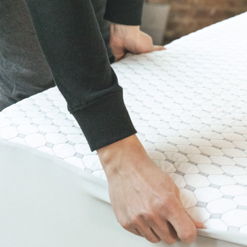 Photo of a person fitting a mattress protector to a mattress.